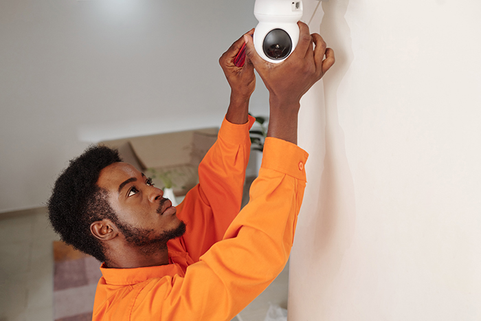 Man in orange shirt adjusting vacation house security camera indoors.