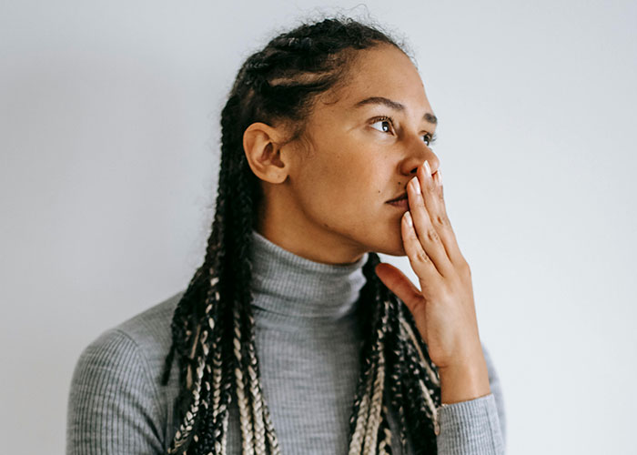 Woman in gray sweater looks pensive, hand covering mouth, reflecting on an anniversary date situation.