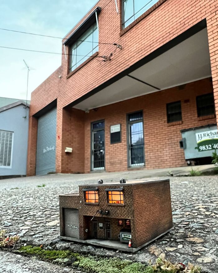 A miniature brick building with glowing windows placed on a city sidewalk, creating a secret world scene.