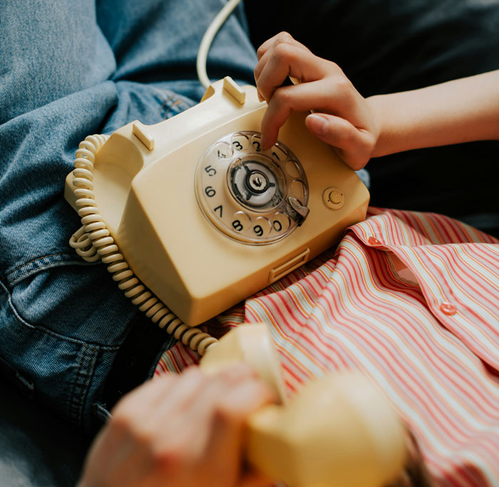 Person dialing a vintage rotary phone while lying on a parent's lap, symbolizing close parent-child connections.