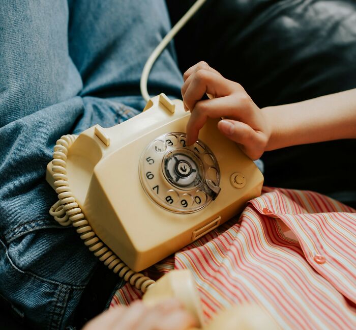 Person dialing a vintage yellow rotary phone, representing activities from 30 years ago.
