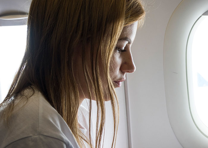 Woman sitting on a plane, looking down, next to a window.