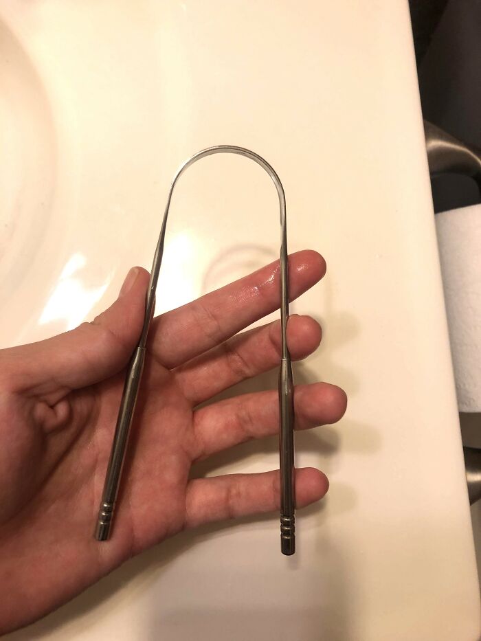 Hand holding a metal tongue scraper, a hygiene tool to keep you smelling fresh.
