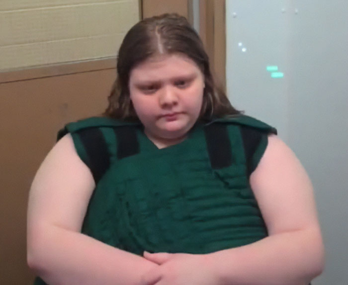 Teen in courtroom wearing a green vest, involved in argument about God.