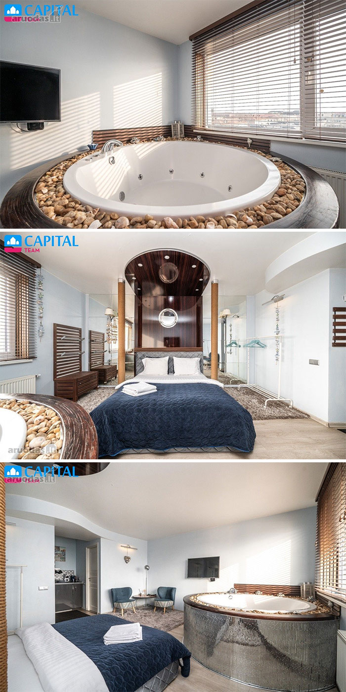 Modern bedroom with a round bathtub surrounded by stones, large windows, and contemporary furnishings in a unique real estate property.