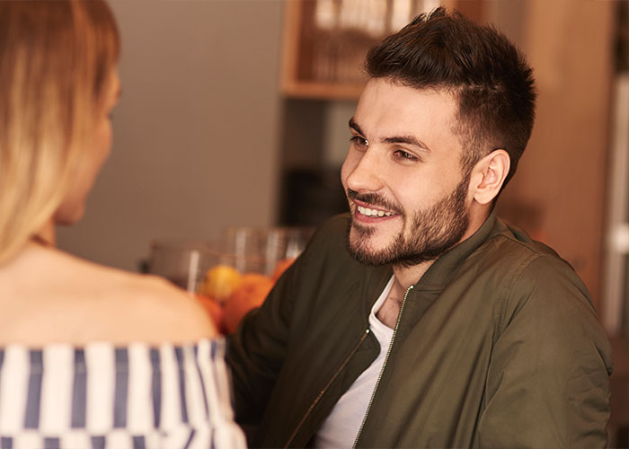 A smiling man sharing a relationship cheat code in marriage while talking to a woman in a casual indoor setting.
