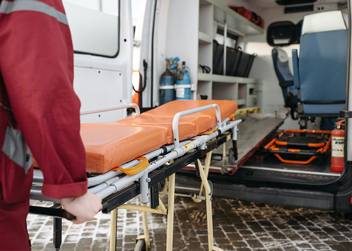 Person in uniform moving stretcher near open ambulance, ready for emergency response.