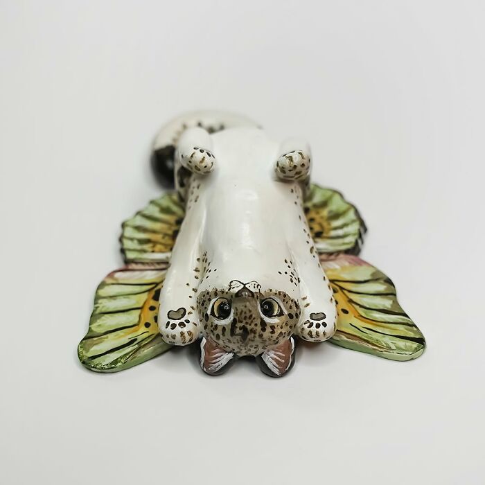 Pocket-sized animal figurine by Vallavica, featuring a playful seal with colorful wings, lying on its back.