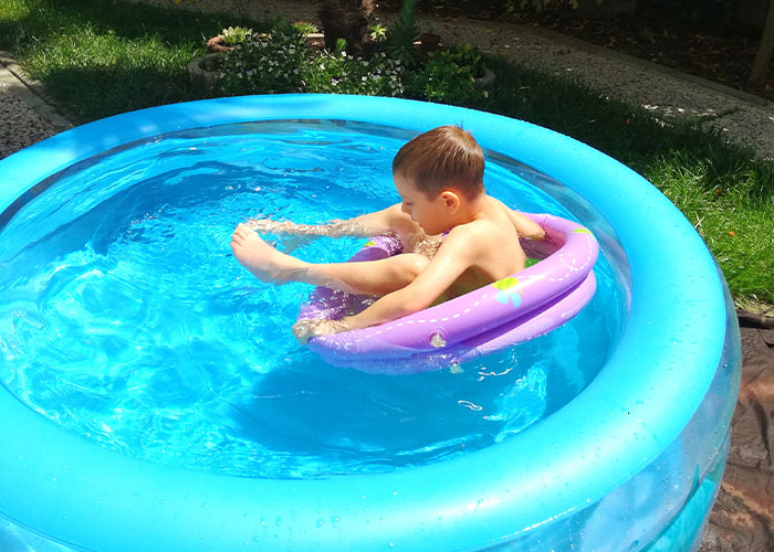 Child in an inflatable pool, enjoying summer outdoors, with vibrant blue water and a purple float, representing HOA challenges.