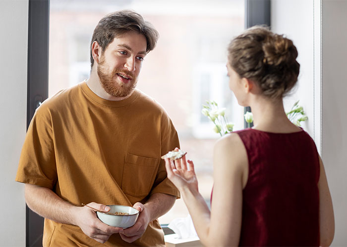 Man in a brown shirt holding a bowl, talking to a woman, capturing a moment of interaction and connection.