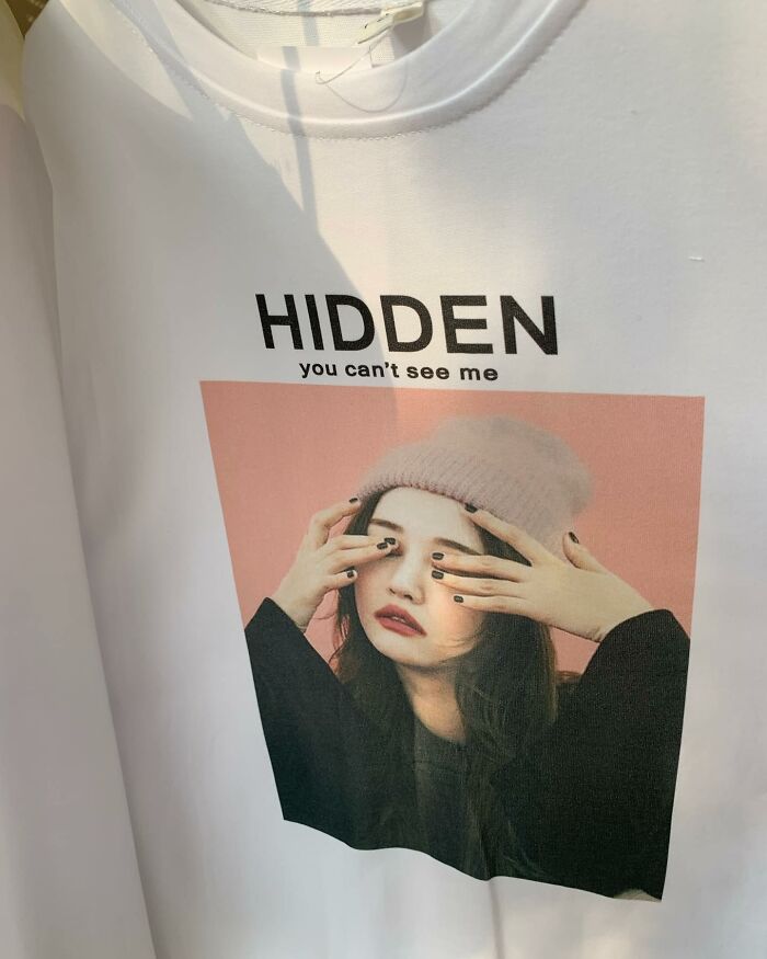 T-shirt with amusing lost translation text "HIDDEN, you can't see me" featuring a woman covering her eyes.