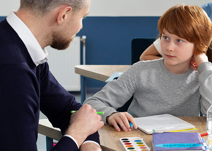 A teacher and student in a classroom, the student holding a paintbrush and looking concerned.