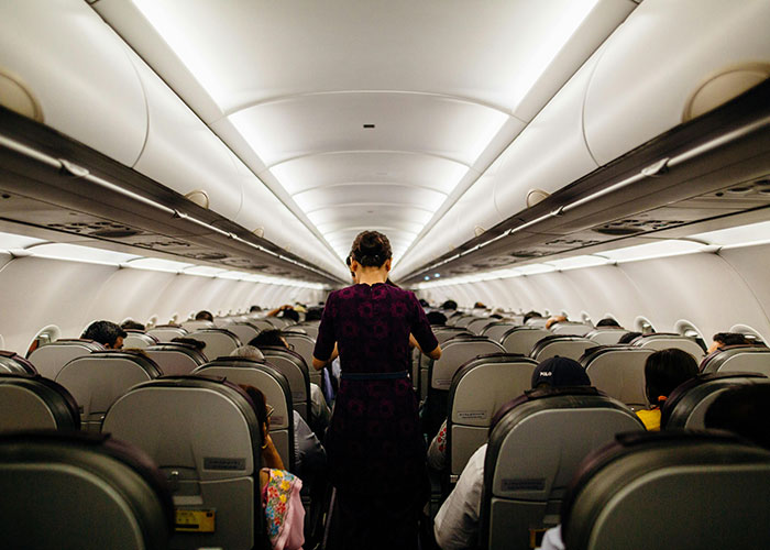 Flight attendant walking down airplane aisle, passengers seated.