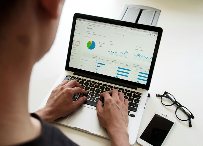 Person analyzing SEO deliverables on a laptop showing website traffic and data charts in a bright workspace.
