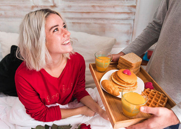 Woman smiling at partner serving breakfast in bed, illustrating a cheat code discovered in marriage that actually works.