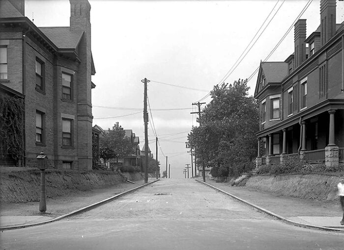 Early 20th century American street scene with telephone poles, trees, and residential houses showing life in America from 100 years ago.