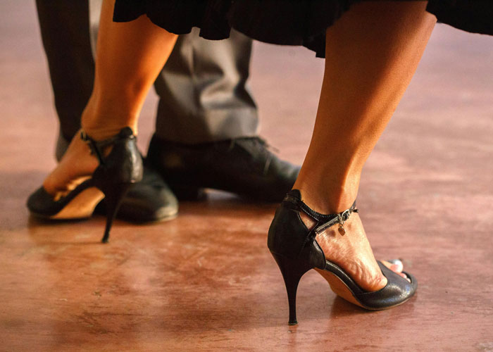 Couple dancing closely, wearing elegant shoes on a polished wooden floor.