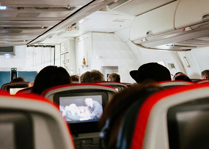 Passengers seated on a plane with monitors showing a movie, highlighting a "You've Gotta Be Kidding Me" moment.