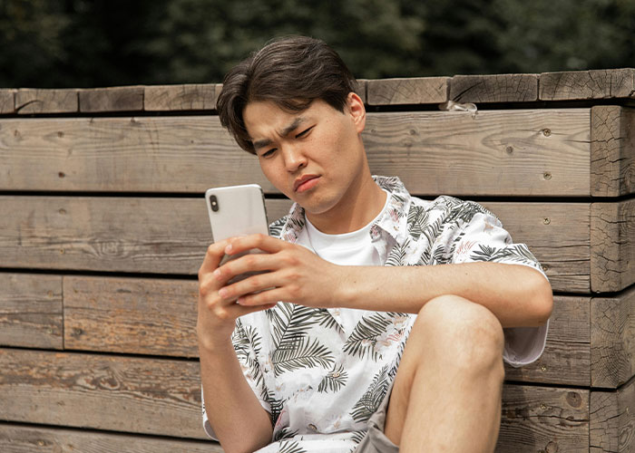 Young man looking heartbroken and confused while checking his phone outdoors, illustrating signs of cheating in relationships.