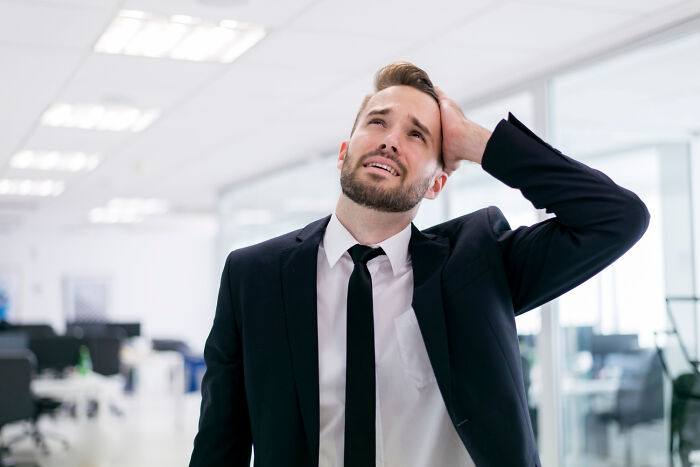 A frustrated man in a suit in an office, likely witnessing work drama.