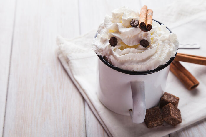 Mug of affordable treats topped with whipped cream and cinnamon sticks on a wooden table.