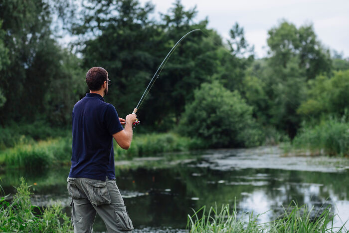 Man fishing by a calm river surrounded by green trees, illustrating peaceful moments despite relationship arguments.