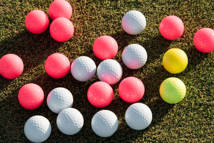 Assorted pink, white, and yellow golf balls scattered on grass, symbolizing diverse and ridiculous job interview questions.