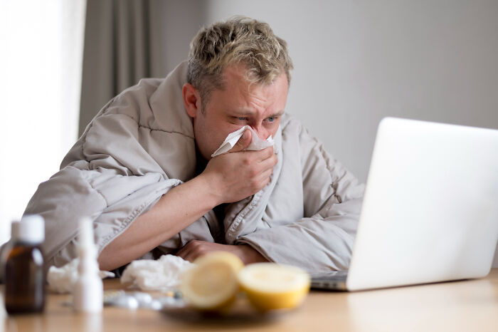 A person wrapped in a blanket, using a laptop, highlighting American habits while feeling unwell.