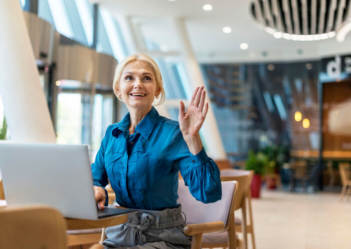 A woman in a modern office waves hello, embodying work drama with her expressive gesture.