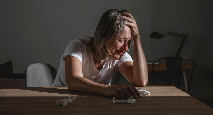 A woman appears distressed at a table, hand on her head, deep in thought about the scariest things out there.