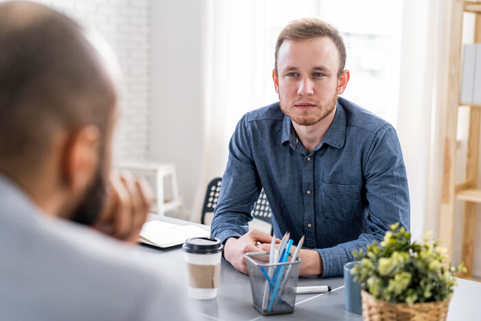 Man in blue shirt answering ridiculous questions during a job interview in a modern office setting.