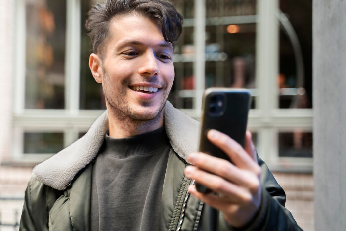Person smiling while looking at a smartphone, capturing dramatic work moments.