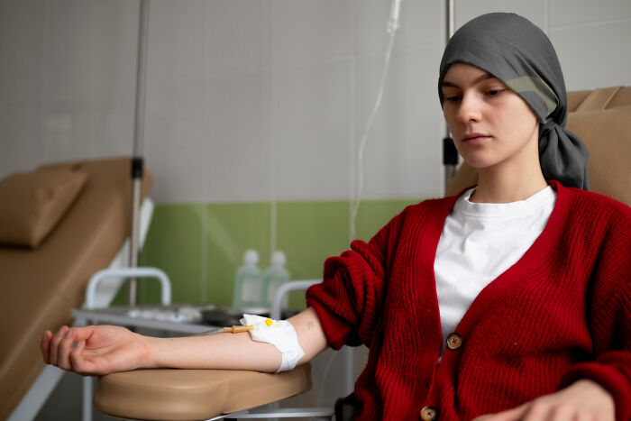 Person in a medical setting, receiving IV therapy, wearing a red sweater and grey headscarf, depicting a scary scenario.