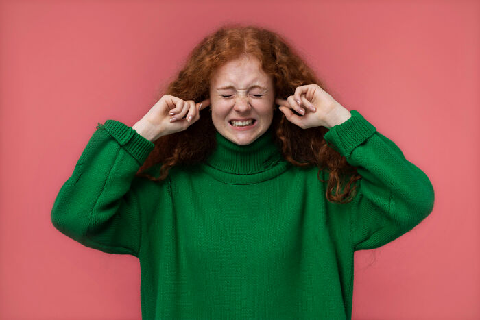 Person in a green sweater covering ears, conveying frustration linked to parents regretting picking favorites.