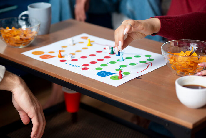 People playing a colorful board game, drinks and snacks on the table, during a lively high school gathering.