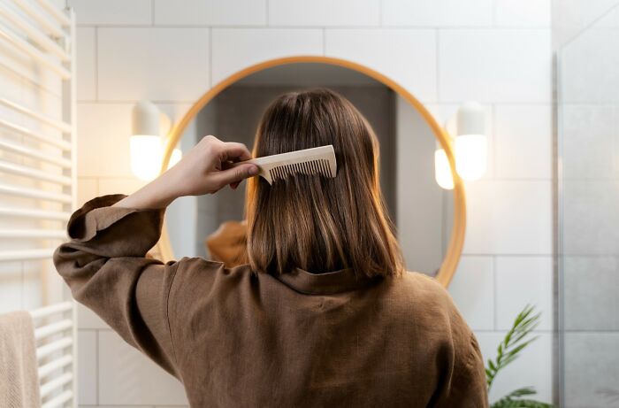 Woman brushing hair in front of round mirror, exploring aspects of relationships and beauty routines.