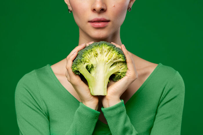 Person in green shirt holding broccoli, against a green background, evoking bizarre house decor themes.