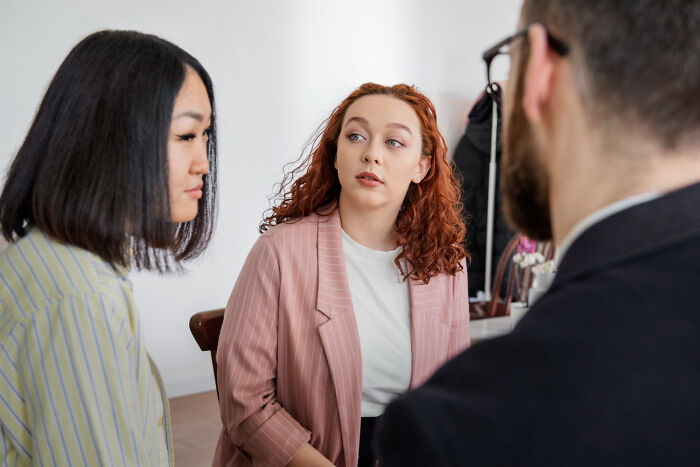 Three people in a job interview setting, discussing and reacting to ridiculous questions asked during interviews.