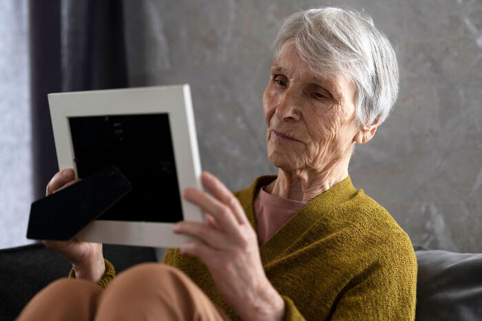 Elderly woman contemplating a framed photograph, illustrating harsh realities of aging.