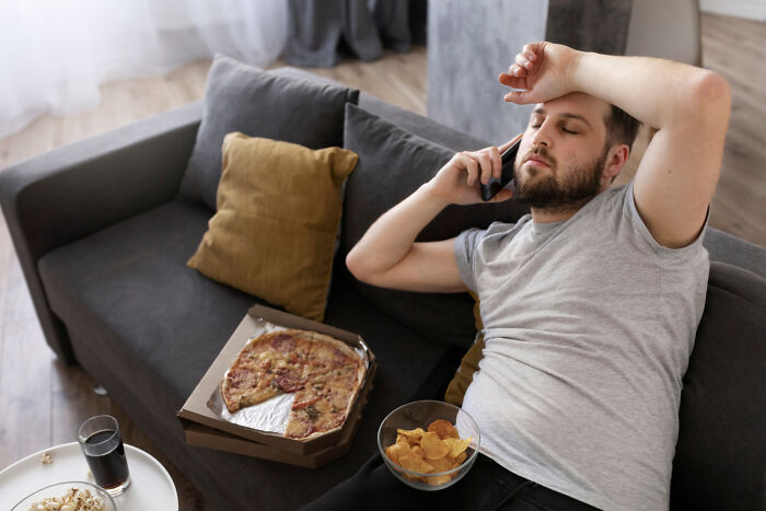 Person relaxing on couch, talking on phone, with pizza and chips nearby.