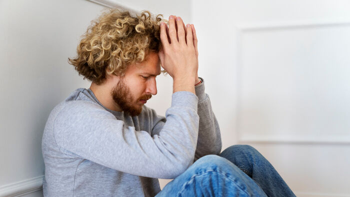 Man sitting against a wall, looking stressed, symbolizing harsh realities of aging.