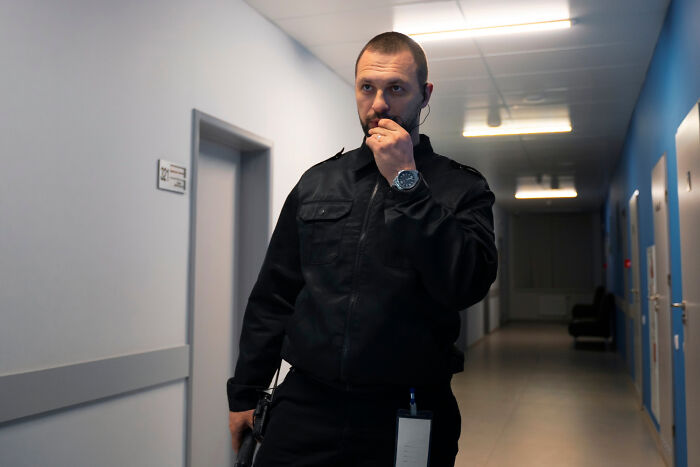 Security guard in a dimly lit hallway, looking alert during an intense workday drama.