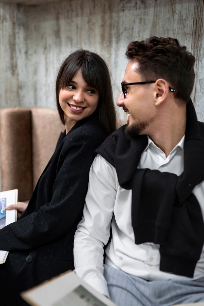 Two colleagues share a laugh, capturing a moment of unhinged work drama in a casual office setting.