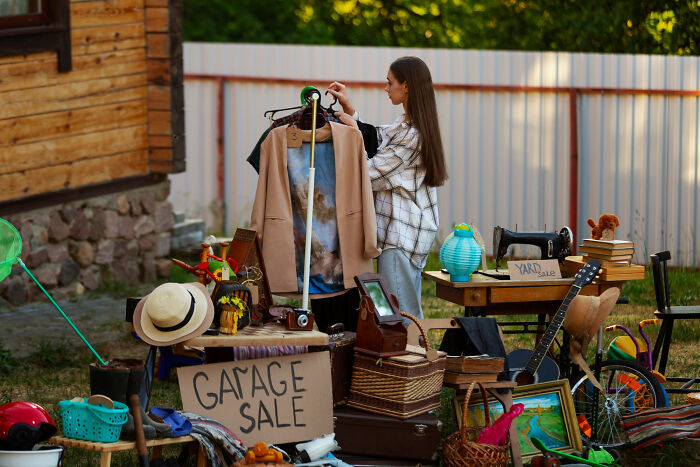A woman browsing clothing at a garage sale filled with affordable treats and miscellaneous items.