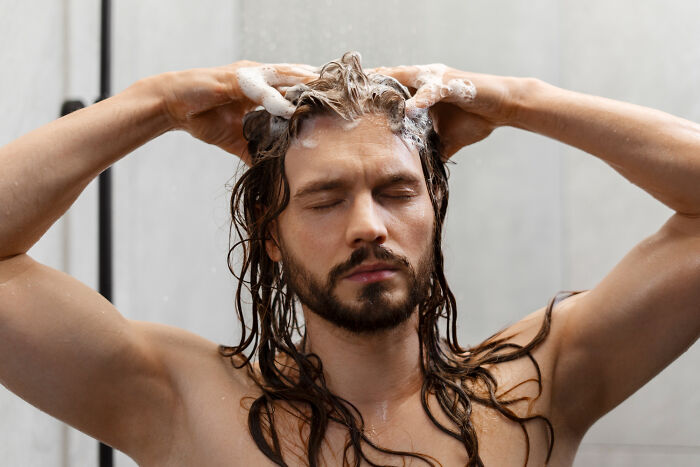 Man showering with eyes closed, lathering shampoo in hair, representing different species in dating experiences.