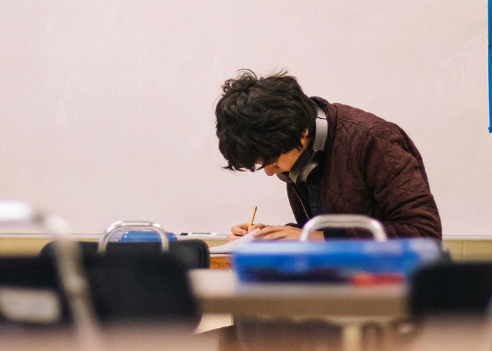 Student writing at a desk in a classroom setting, focused on working.