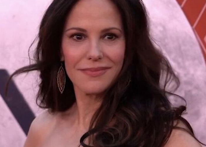 Celebrity posing in a brown dress at a red carpet event, showcasing a friendly demeanor.