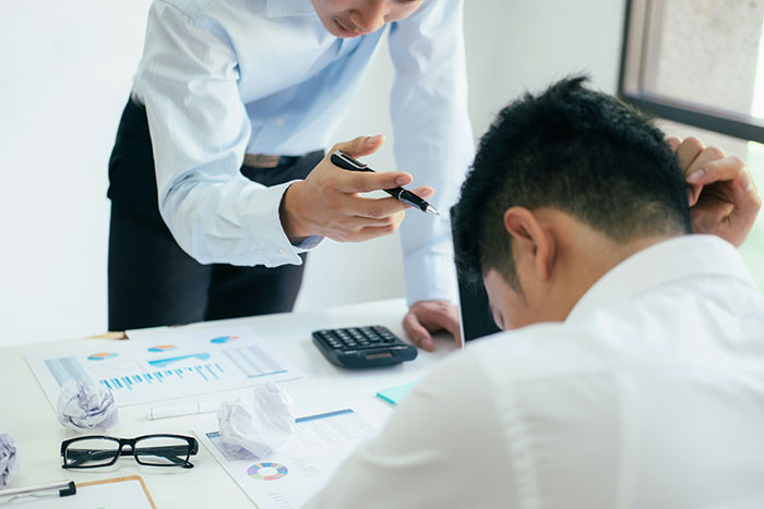 Two office workers discussing SEO deliverables, surrounded by charts, papers, and a calculator in a bright workspace.
