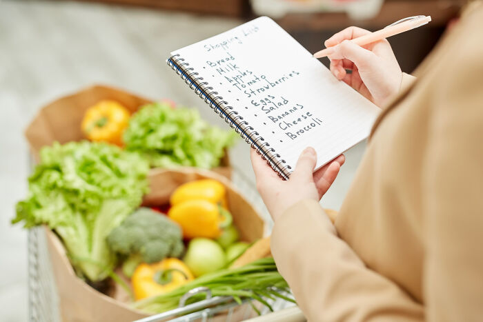Person holding a notebook with a shopping list, surrounded by fresh vegetables, related to relationship arguments topic.