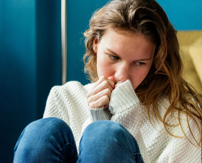 A person in a thoughtful pose, wearing a white sweater, next to a blue wall, illustrating close family relationships.